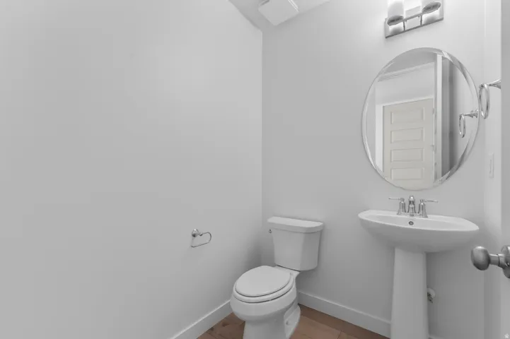 Pedestal sink with chrome faucet, oval mirror, wall-mounted light fixture, and wood-finish flooring