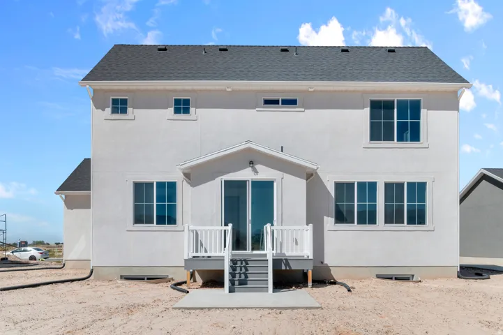 Stucco exterior with a dark shingle roof, featuring multiple windows, a covered deck with white railing, and sliding glass doors