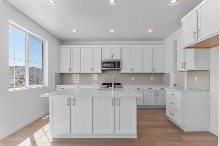 Kitchen featuring white cabinetry, light-toned wood-finish flooring, recessed lighting, and a kitchen island with a built-in sink