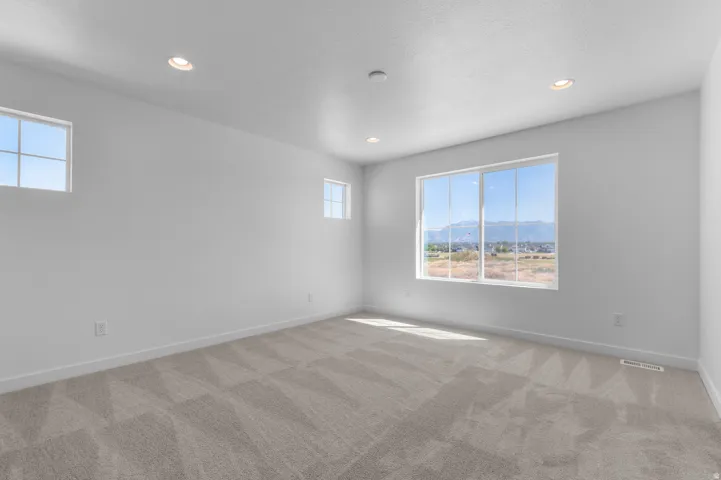 Recessed ceiling lighting, multiple windows, light-toned carpeting, and white walls