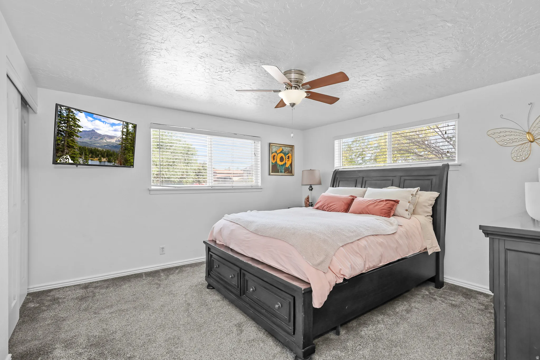 Spacious room featuring neutral carpeting, a ceiling fan with integrated lighting, and two large windows with blinds