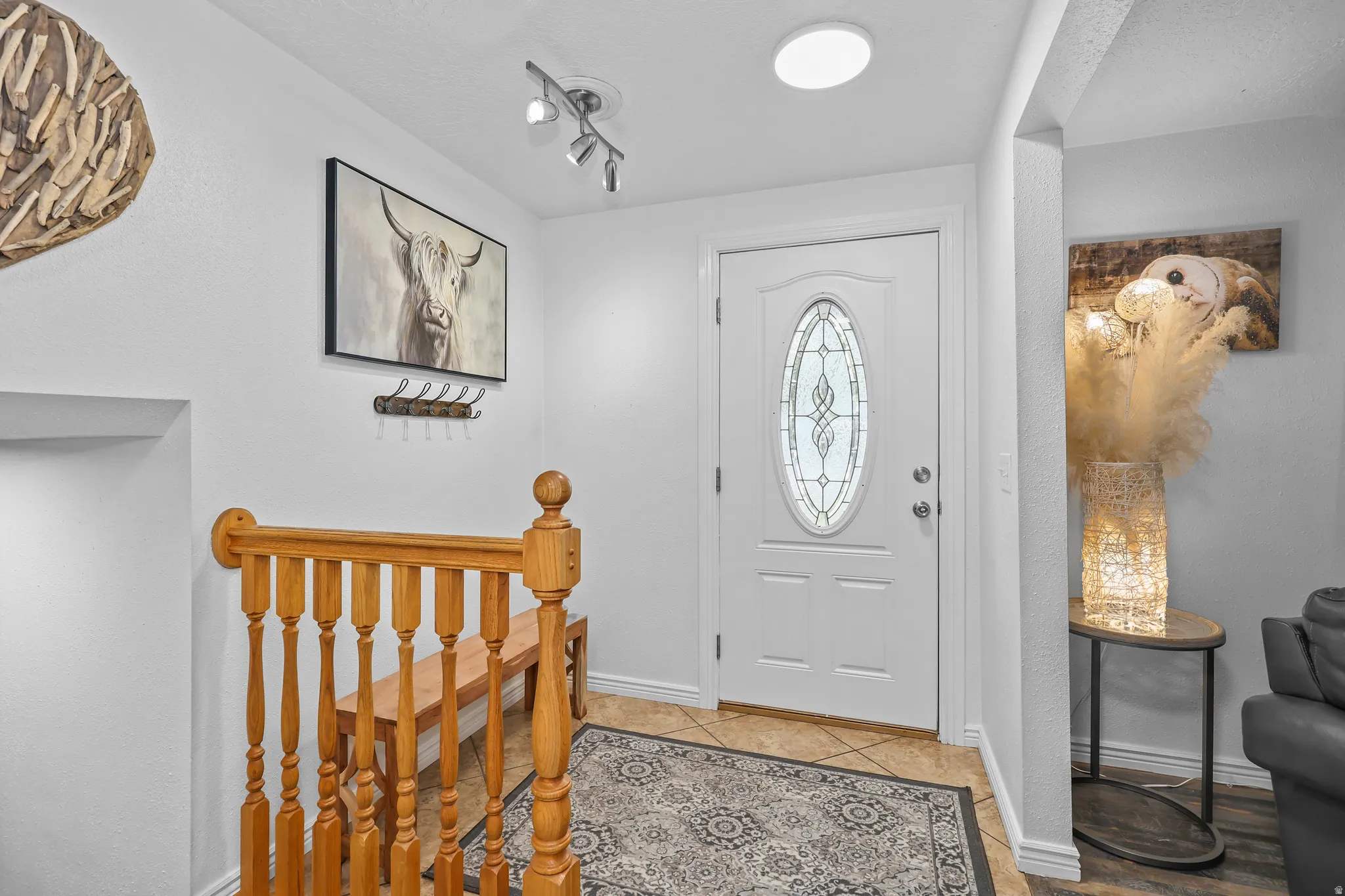 Entryway featuring a white paneled door with an oval stained-glass insert, tile flooring, a recessed ceiling light, and a wooden staircase with balusters