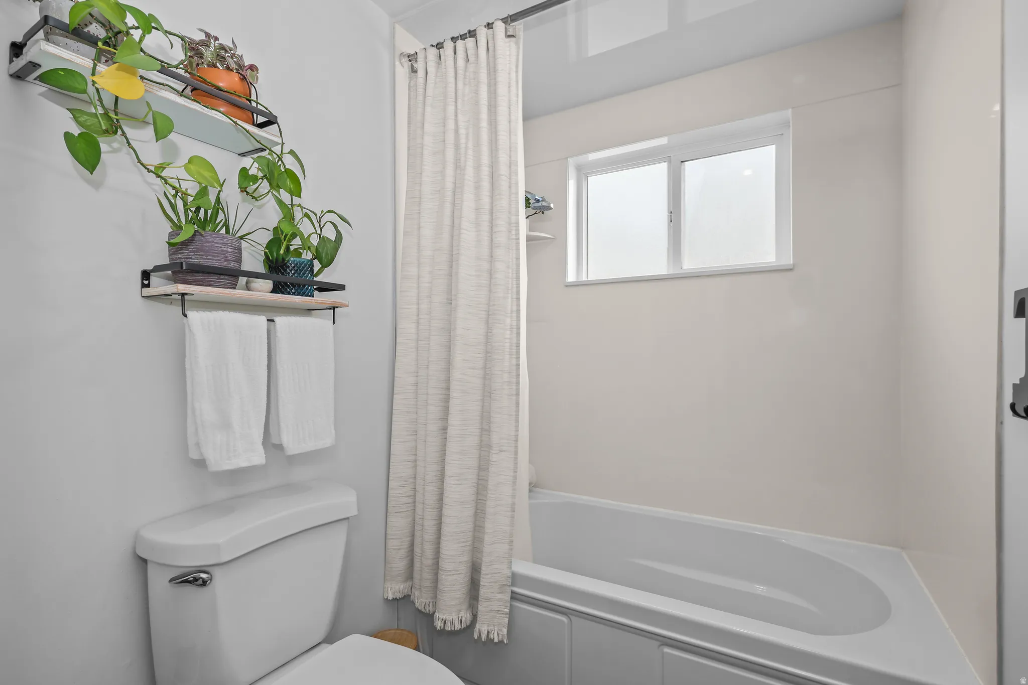 Bathroom featuring a white bathtub, a window above the tub, and a white toilet