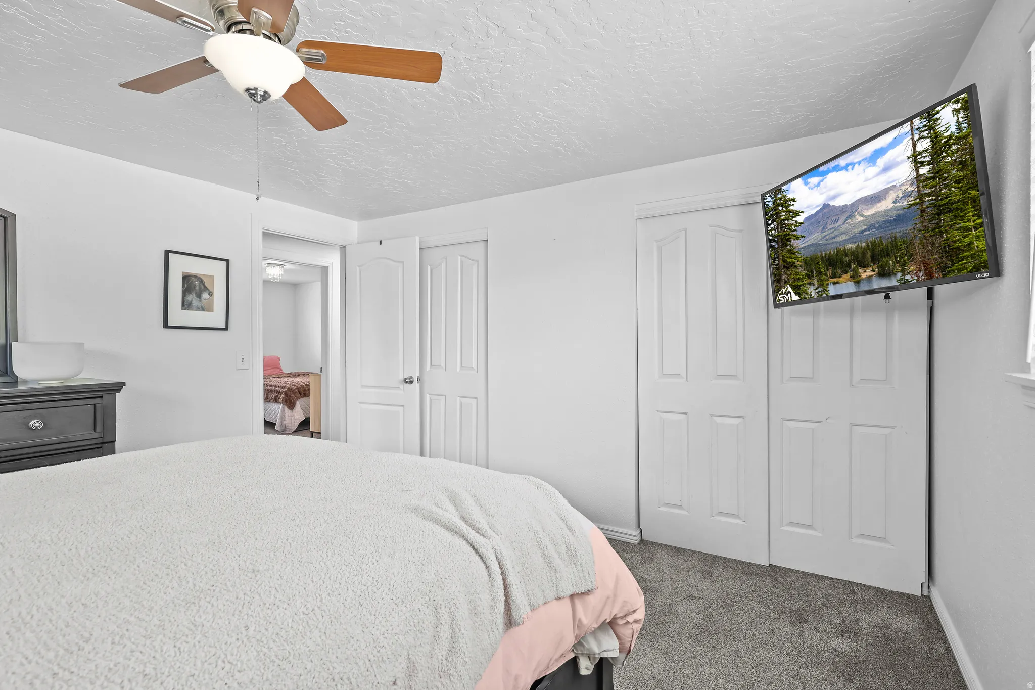 Carpeted bedroom with a ceiling fan, white walls, and a window