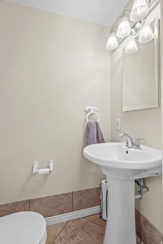 Pedestal sink with chrome faucet, complemented by a large wall-mounted mirror and a four-light fixture