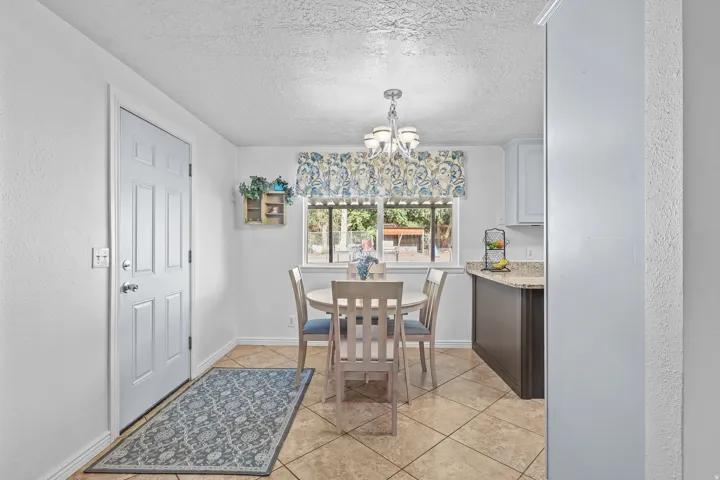 Tiled flooring throughout this dining area, featuring a window with an exterior view, a multi-light chandelier, a paneled door, and a partial view of kitchen cabinetry with a light-colored countertop
