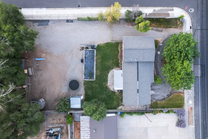 Property featuring a grey shingle roof, a large unpaved area, a rectangular garden bed, and a circular ground-level structure