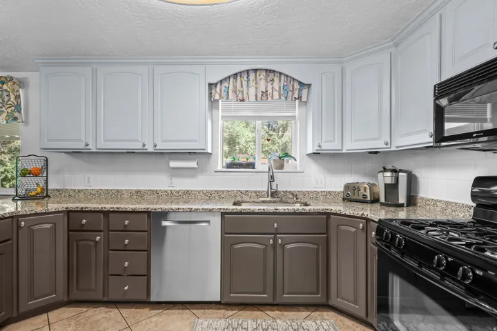 Kitchen featuring two-tone cabinetry, a stainless steel sink with a high-arch faucet, a four-burner gas range, and granite-finish countertops