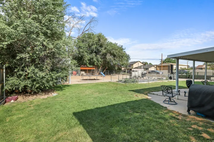 Spacious backyard featuring a covered patio, extensive lawn, mature trees, and a garden bed