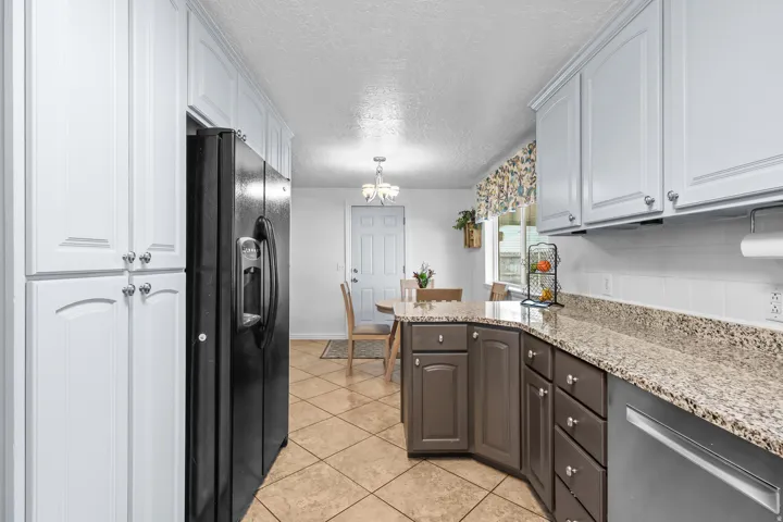 Kitchen featuring a peninsula with granite countertops, a white subway tile backsplash, and light brown lower cabinetry