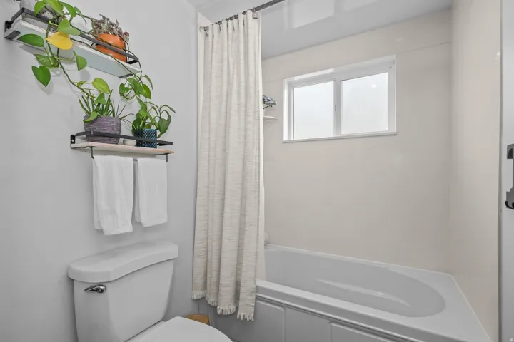 Bathroom featuring a white bathtub, a window above the tub, and a white toilet