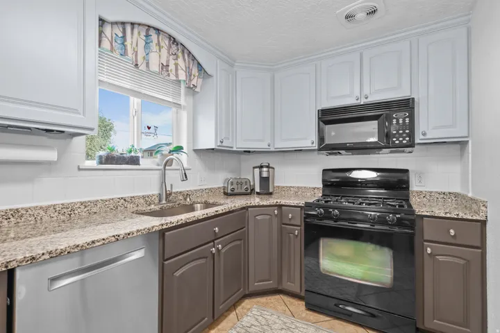 Functional kitchen featuring two-tone cabinetry, a stainless steel sink with a gooseneck faucet, light-toned countertops, and a full suite of black appliances, including a range and over-the-range microwave