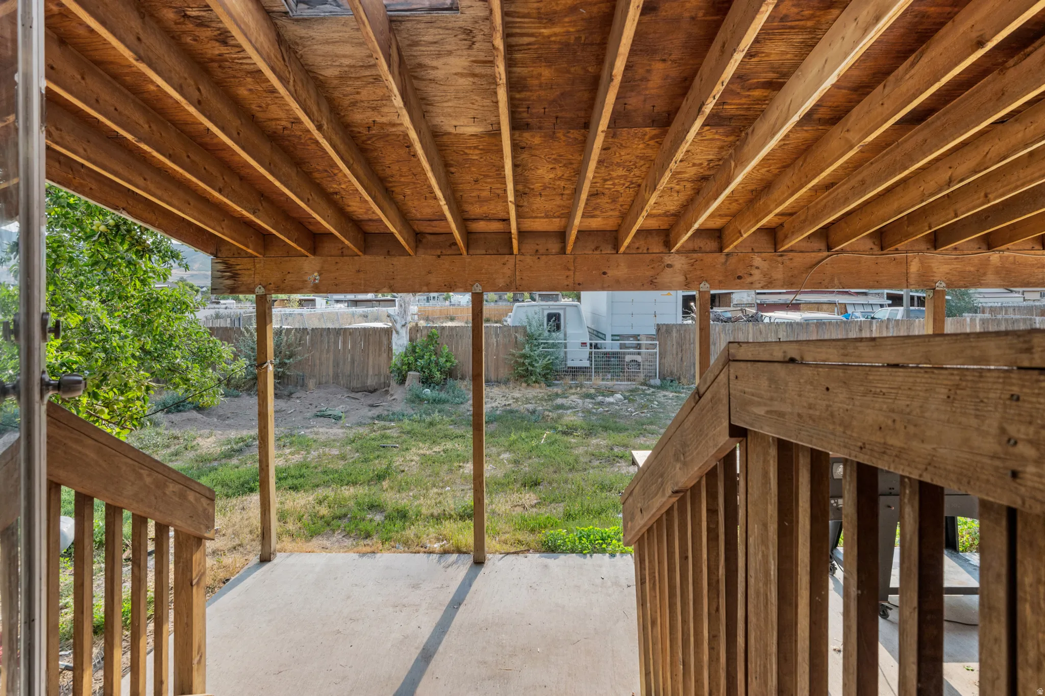 Covered patio area featuring a slatted wood ceiling, wood support beams, wood stair railings, and a concrete patio surface