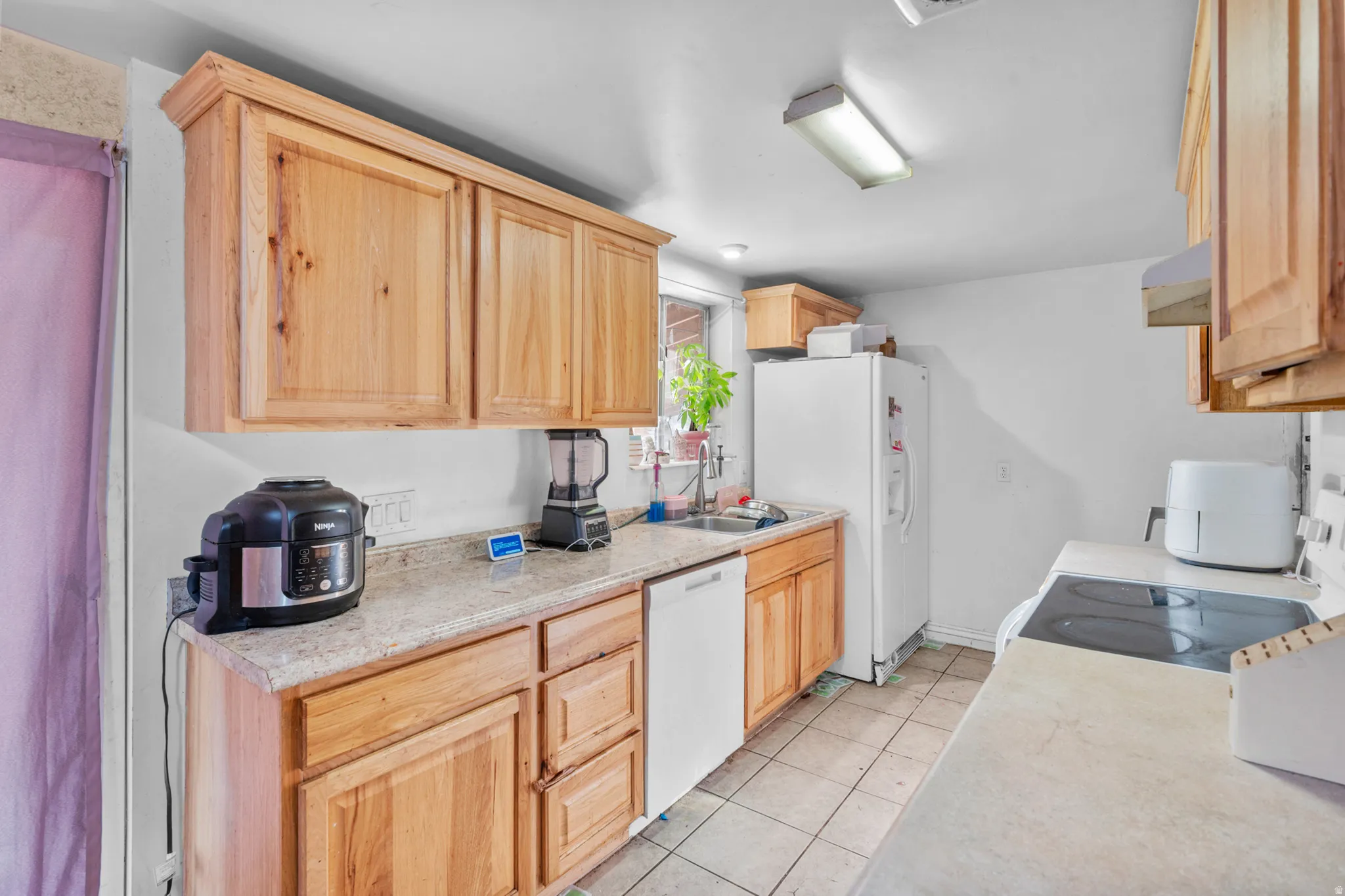 Kitchen featuring natural wood-finish cabinetry, light-toned countertops, and a white dishwasher