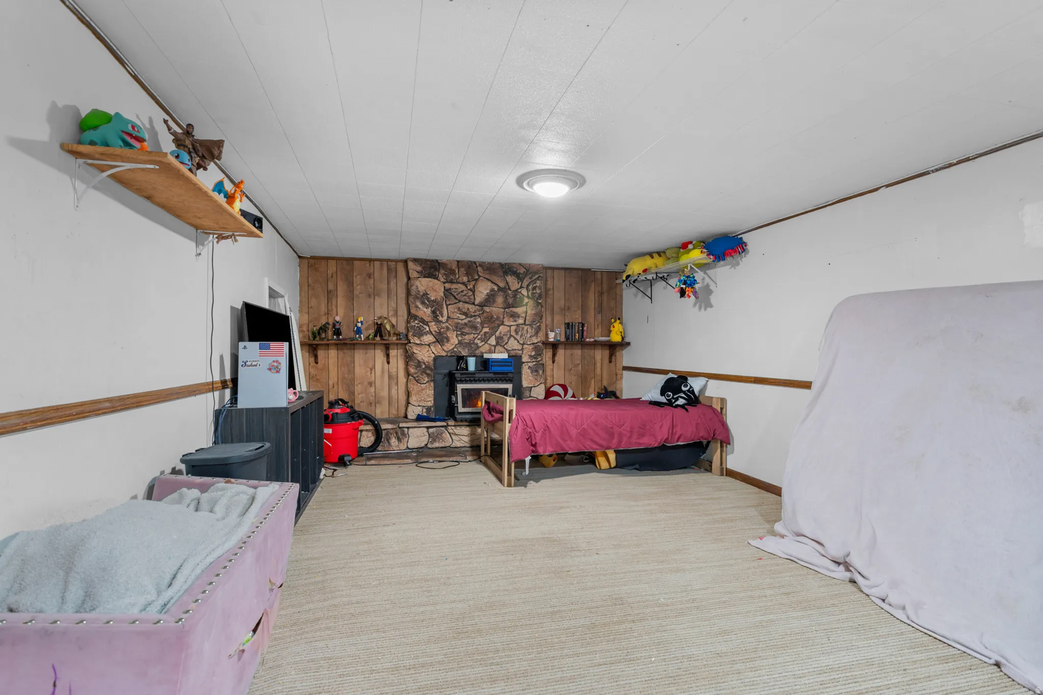 Spacious room featuring a stone-clad fireplace with a wood-panel accent wall and wood mantel