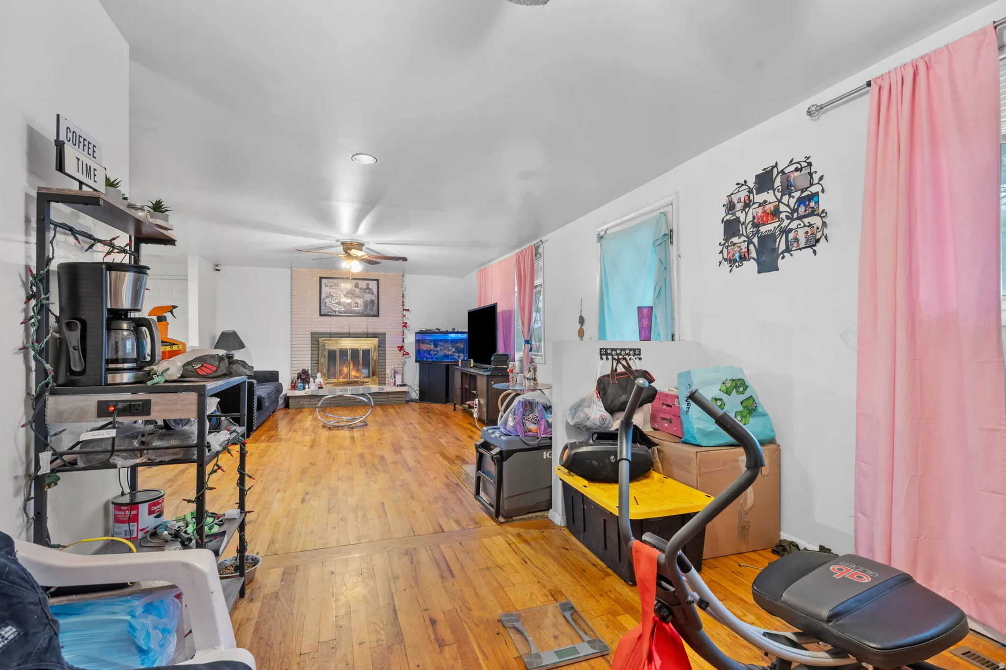 Living room featuring wood-finish flooring, a white brick fireplace, and a ceiling fan