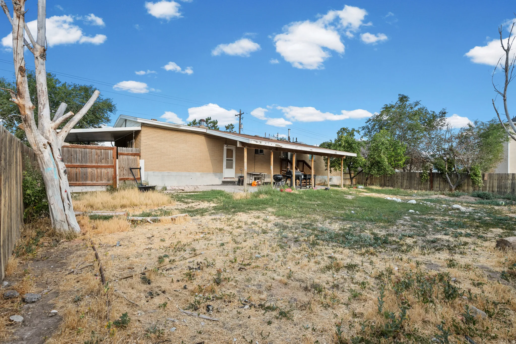 Expansive backyard featuring a partial grass lawn, perimeter fencing, and a covered patio area