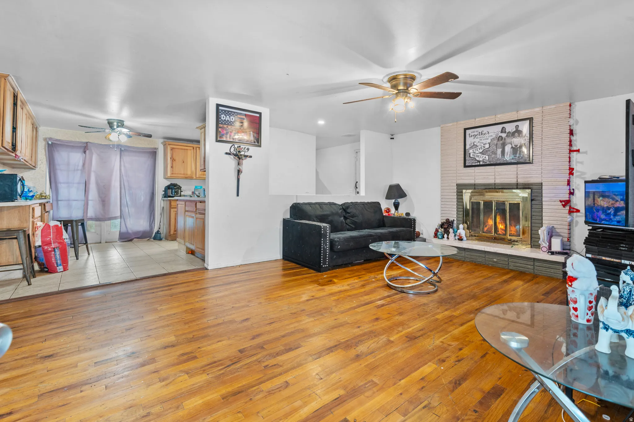 Spacious living area featuring wood-finish flooring, a brick-front fireplace, and a ceiling fan