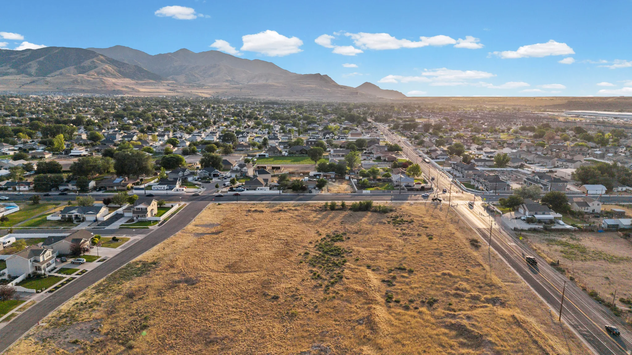 Expansive land parcel featuring direct road frontage, surrounded by established residential areas, and framed by distant mountain ranges