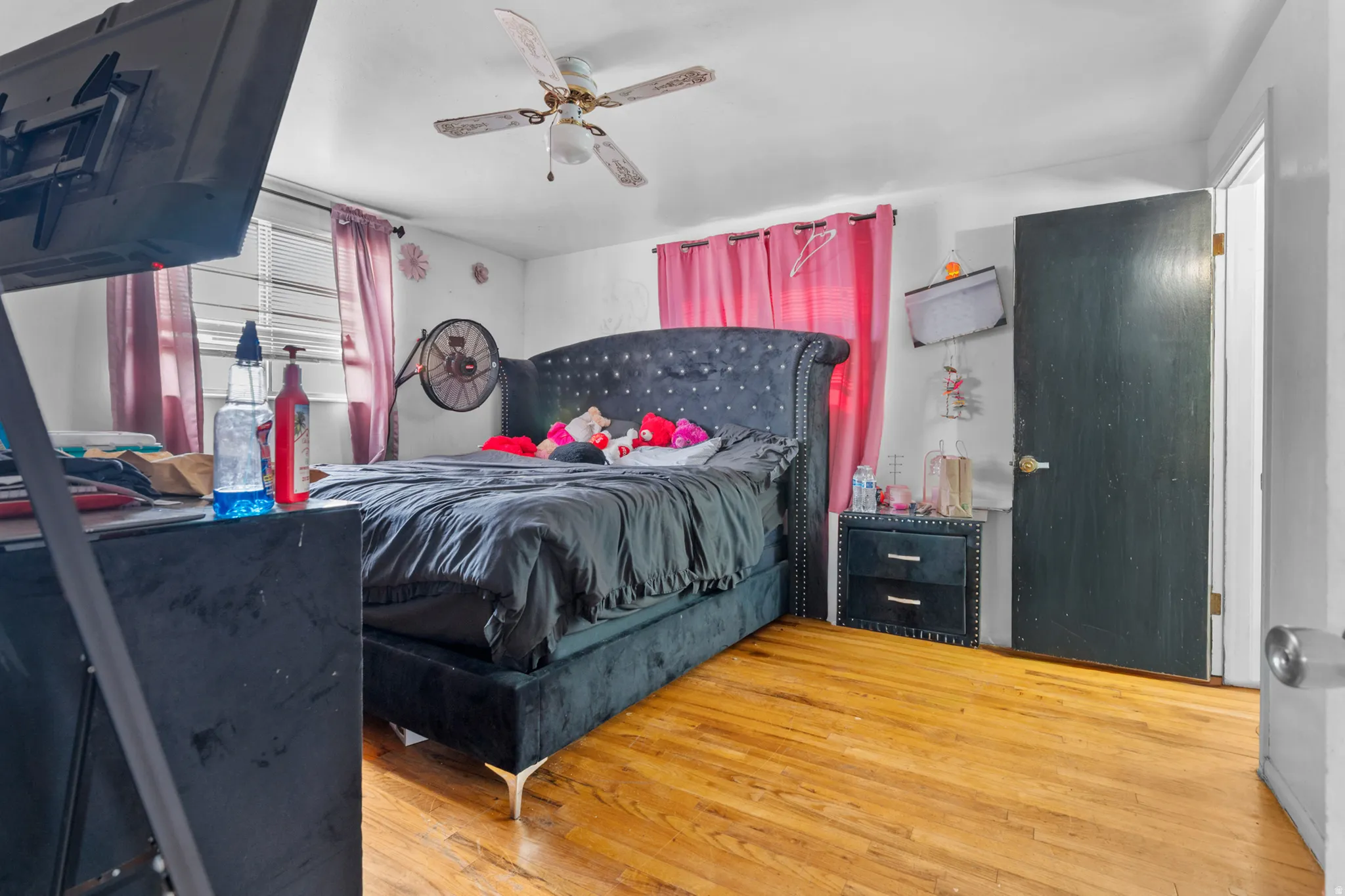 Wood-finish flooring and a ceiling fan are present in this room, featuring a window with blinds