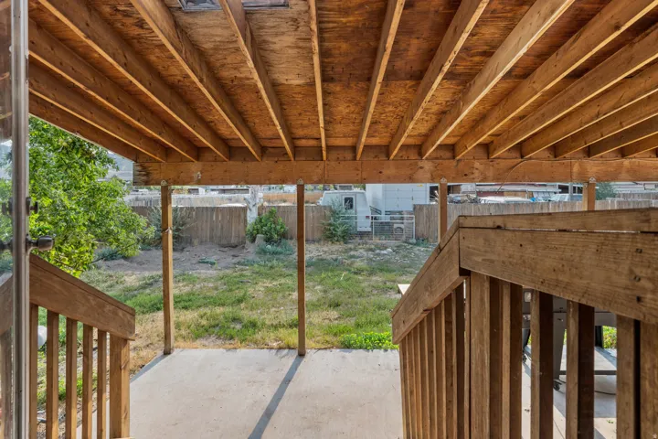 Covered patio area featuring a slatted wood ceiling, wood support beams, wood stair railings, and a concrete patio surface