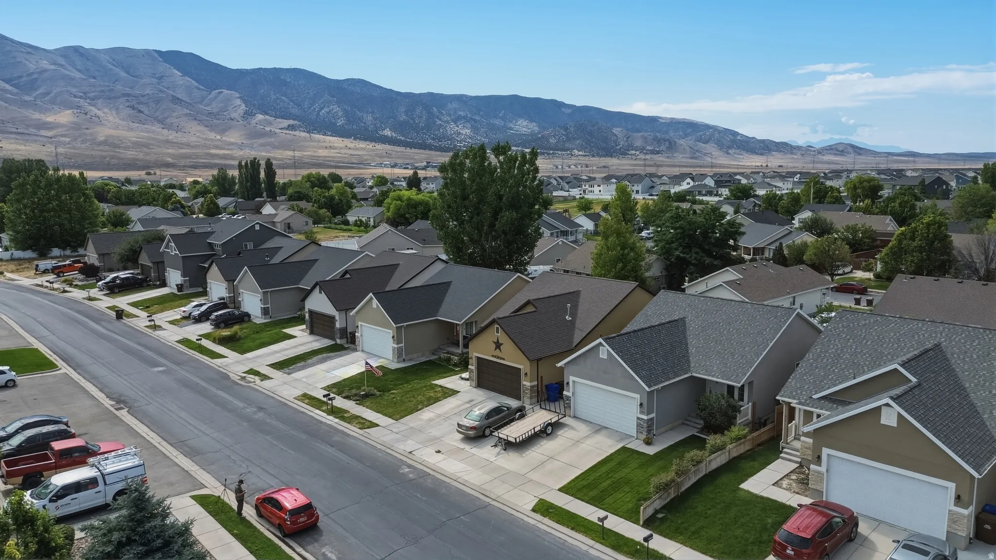 Aerial perspective of a residential street with single-story homes featuring attached garages, pitched roofs, and manicured front lawns
