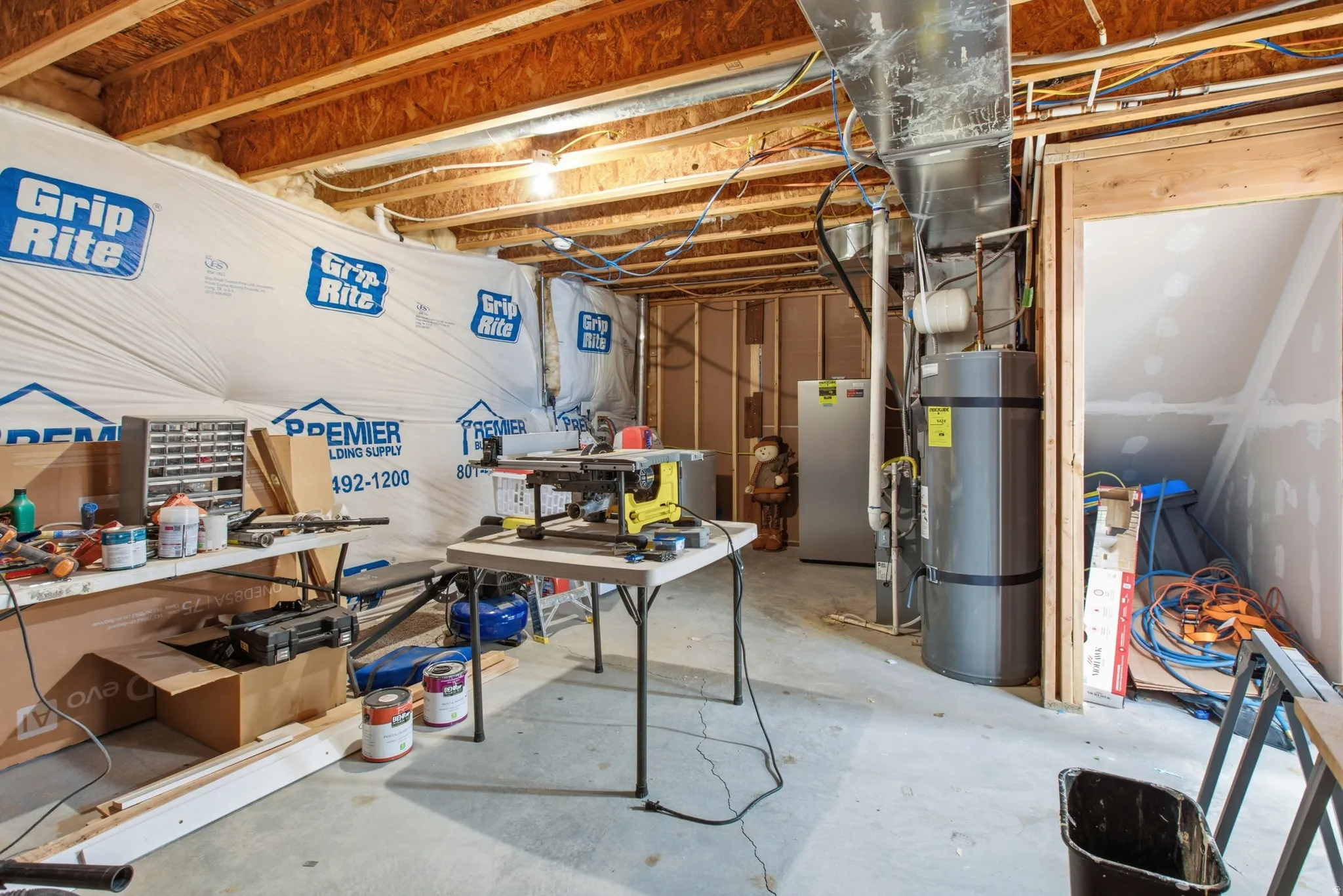 Unfinished basement featuring exposed wood joists, concrete flooring, and a water heater