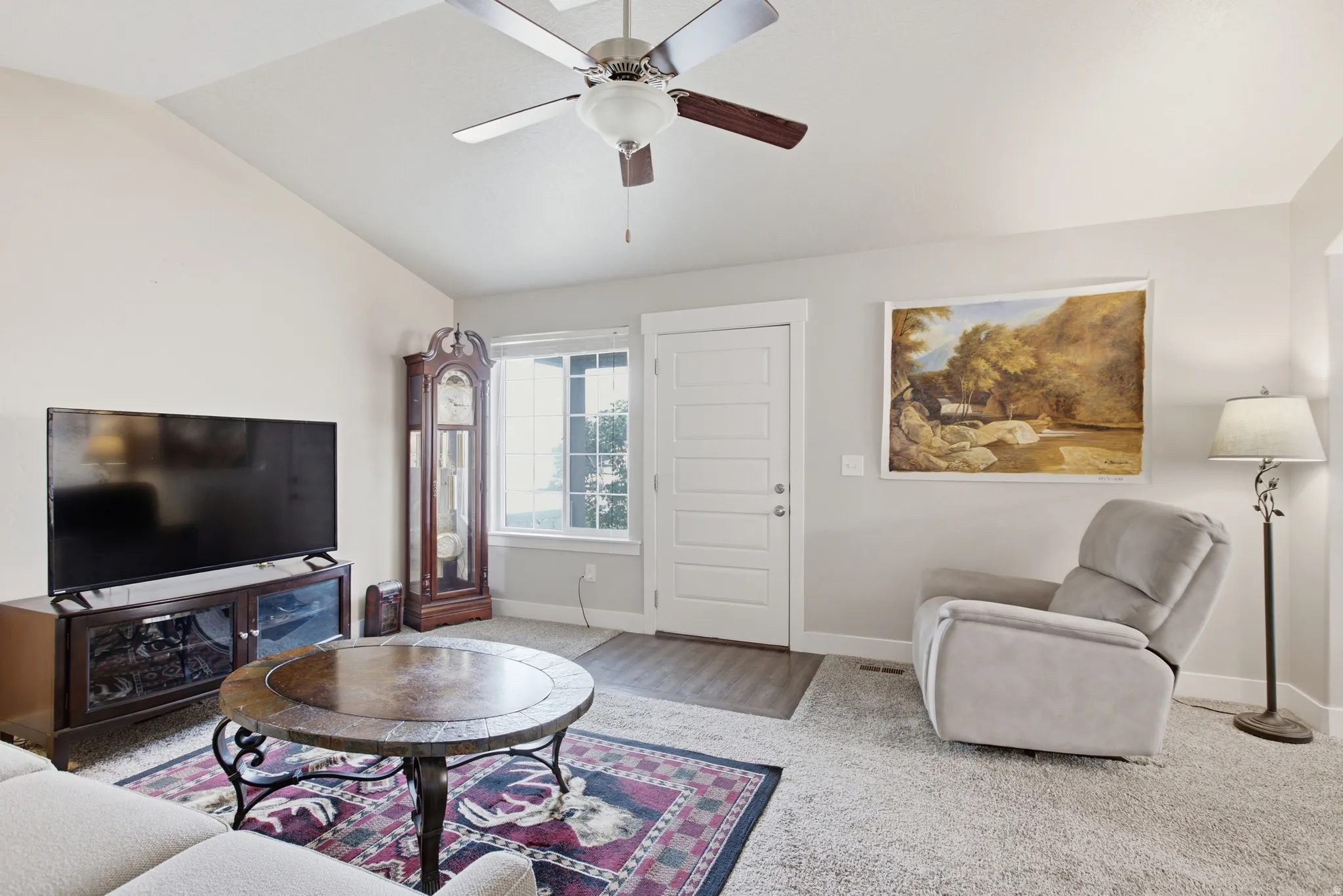 Spacious room featuring vaulted ceilings, a ceiling fan with integrated lighting, window with white trim, a white paneled door, and neutral wall paint