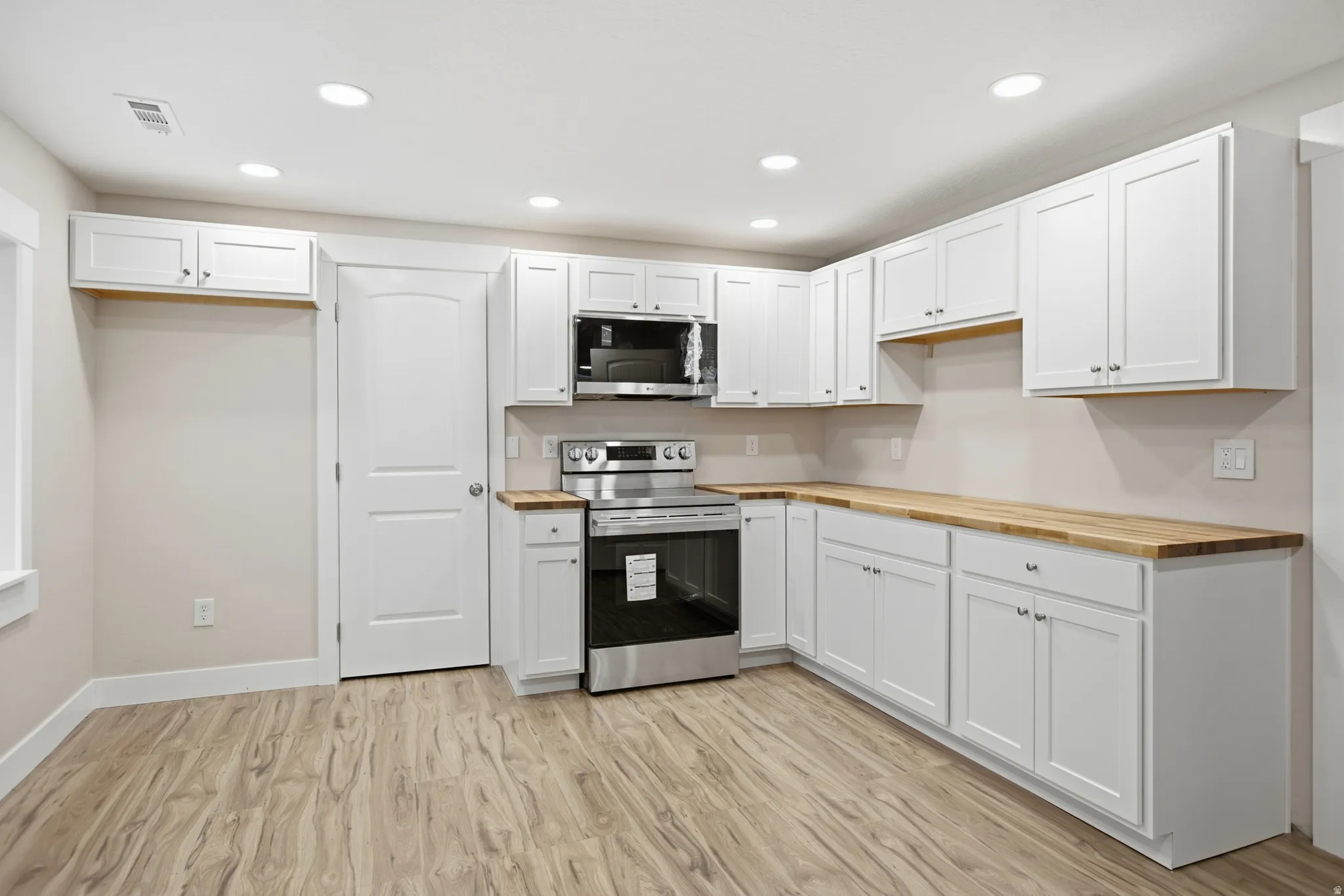 Kitchen featuring extensive white cabinetry, wood-finish countertops, stainless steel range, and overhead microwave