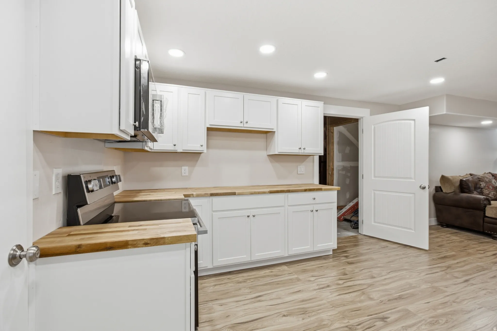 Kitchenette featuring white cabinetry with brushed nickel hardware, wood-finish countertops, and a stainless steel electric range with an overhead microwave
