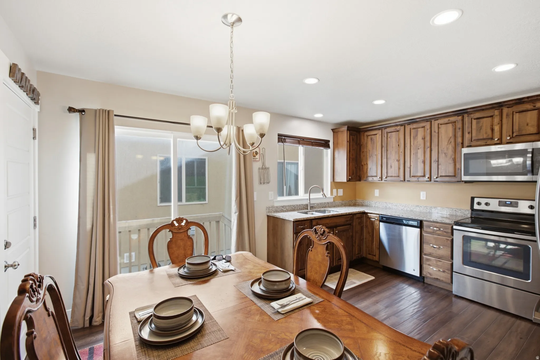 Open-concept dining area with wood-finish flooring, a contemporary chandelier, and direct access to an outdoor balcony