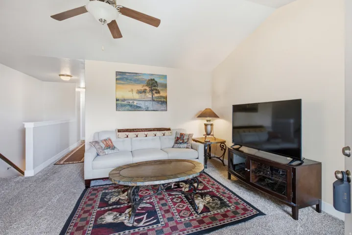 Living area featuring vaulted ceilings, a ceiling fan with wood-finish blades, and neutral-toned wall paint