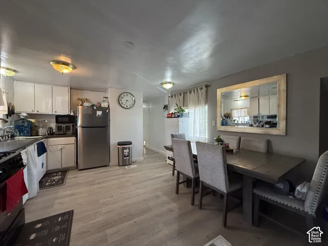 Open-concept kitchen and dining area featuring light wood-finish flooring, white cabinetry, and stainless steel appliances