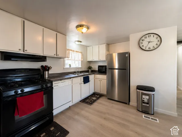Kitchen featuring wood-finish flooring, white cabinetry with silver-tone hardware, dark countertops, and a full suite of appliances including a stainless steel refrigerator and black gas range