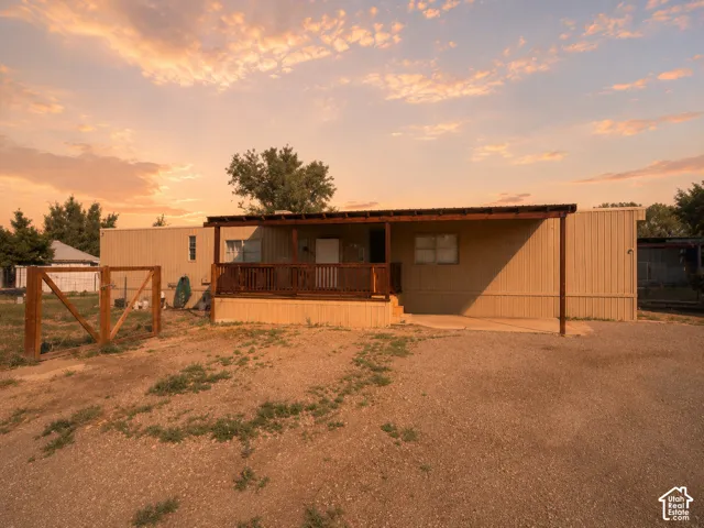 Exterior featuring a covered wooden porch, gravel driveway, and surrounding fence