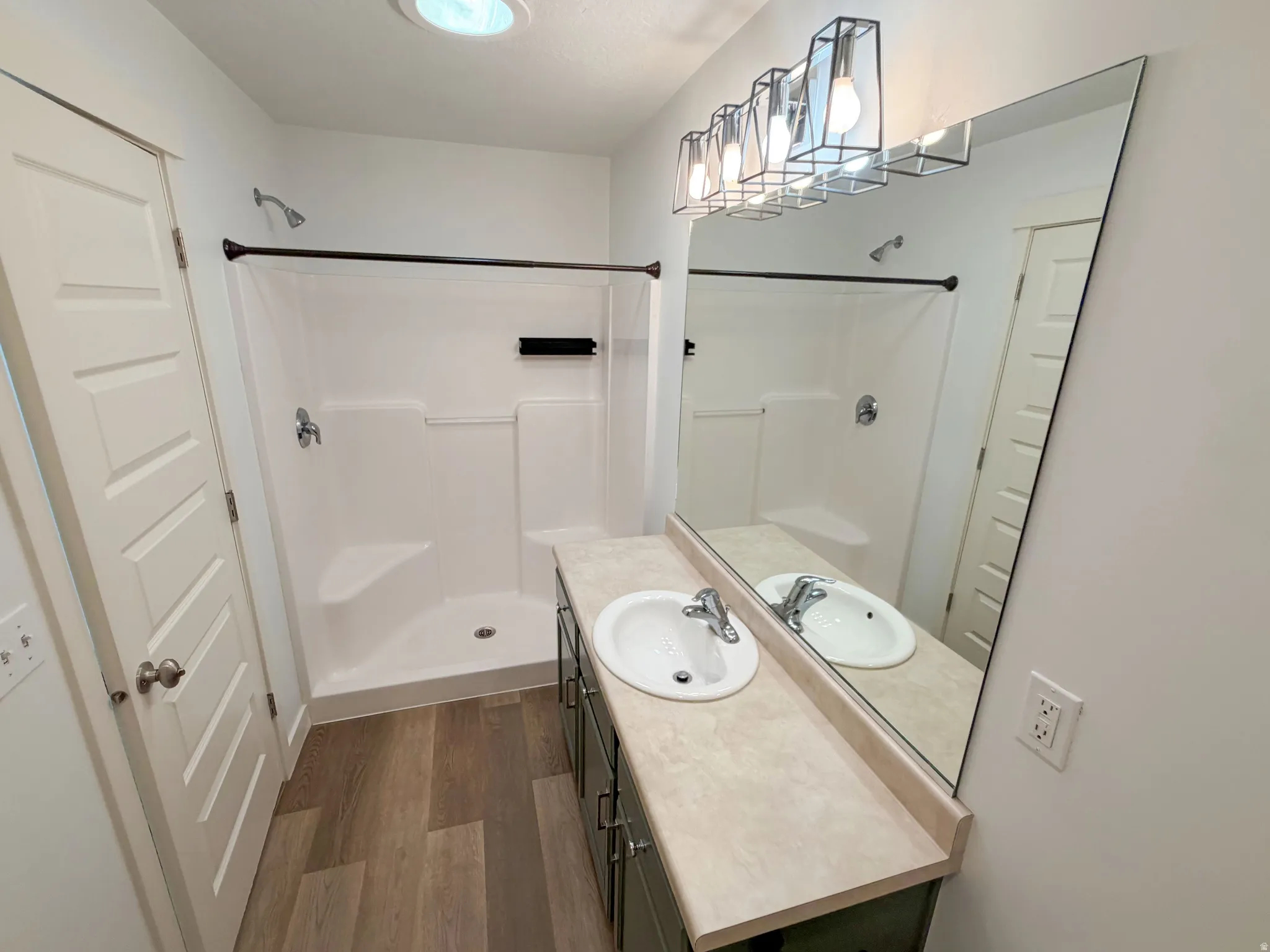 Bathroom featuring a single vanity with a laminate countertop, wood-finish flooring, and a shower stall with an integrated bench