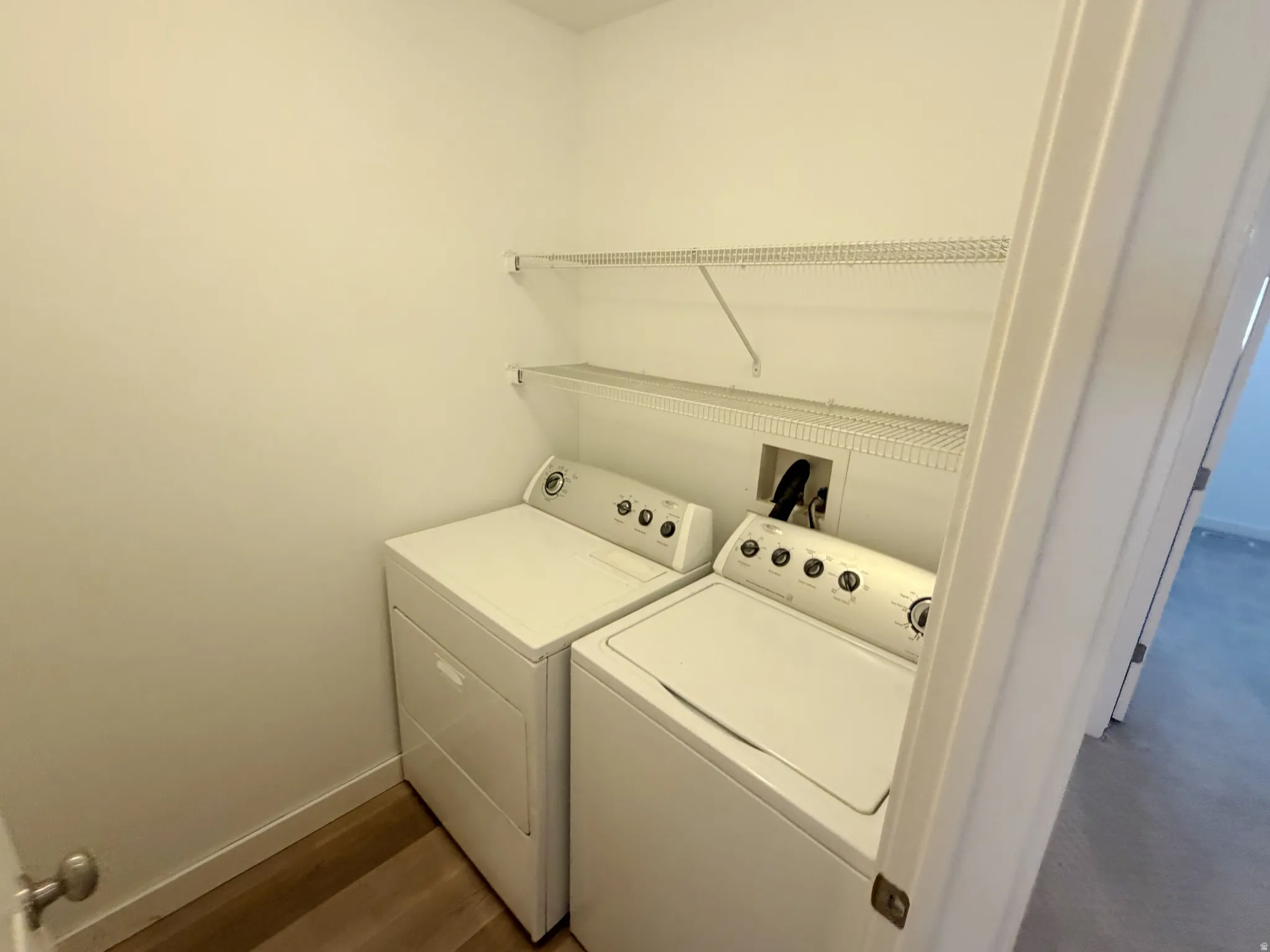 Dedicated laundry area featuring a washer and dryer, wood-finish flooring, white walls, and two wire shelving units