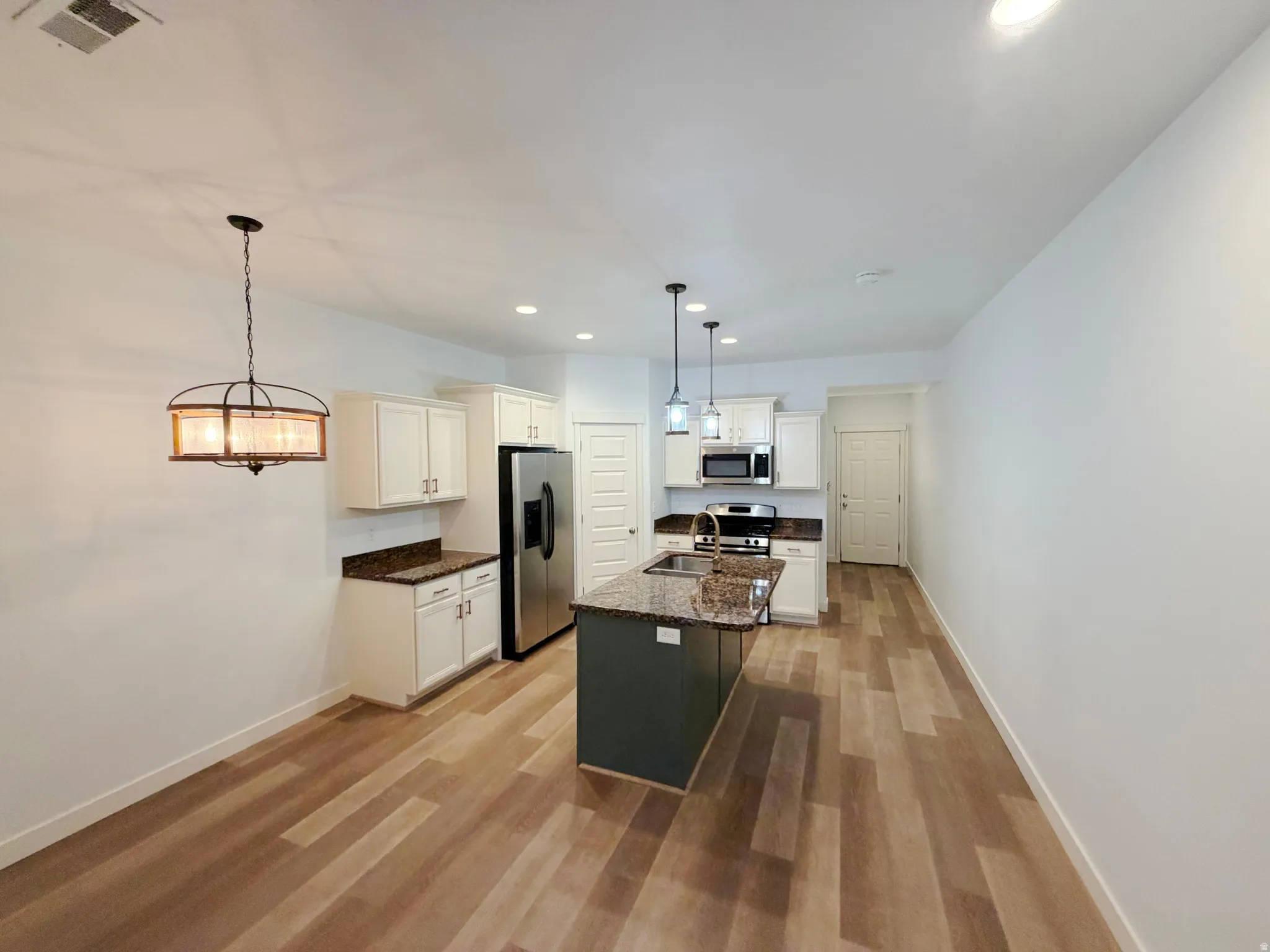 Open-concept kitchen and dining area featuring wood-finish flooring, recessed lighting, and a decorative dining pendant