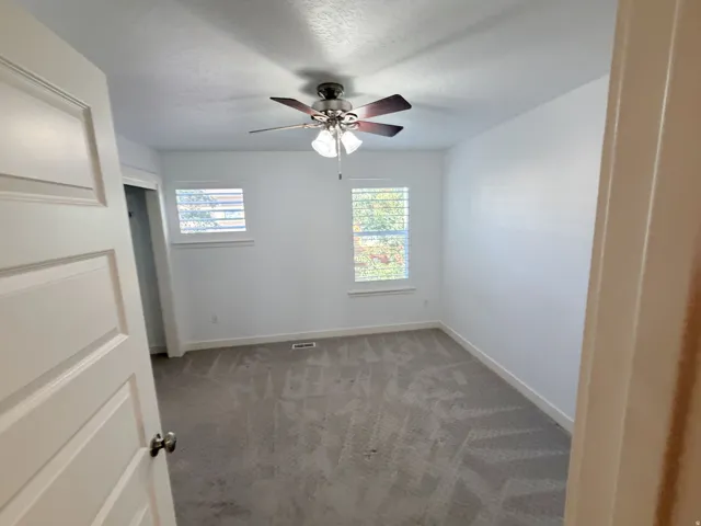 Room featuring neutral-toned carpeting, white walls, and a ceiling fan with integrated lighting