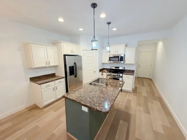 Kitchen featuring a central island with a double basin sink, granite countertops, stainless steel appliances, wood-finish flooring, and recessed lighting