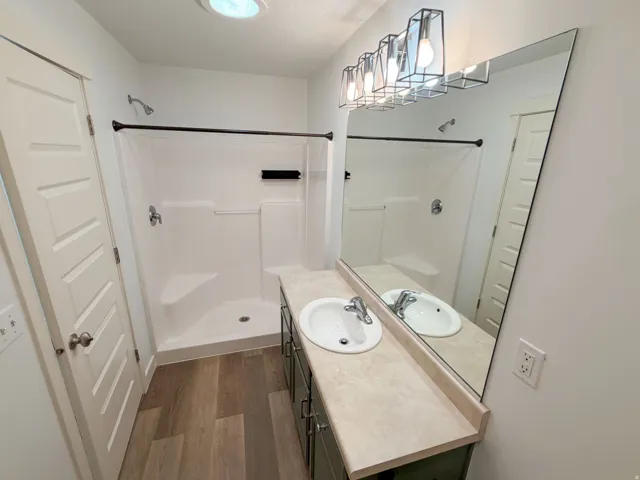 Bathroom featuring a single vanity with a laminate countertop, wood-finish flooring, and a shower stall with an integrated bench