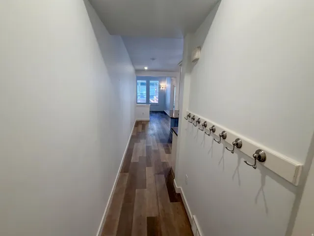 Hallway featuring wood-finish flooring, light-toned walls, recessed lighting, and a wall-mounted coat rack with brushed nickel hooks