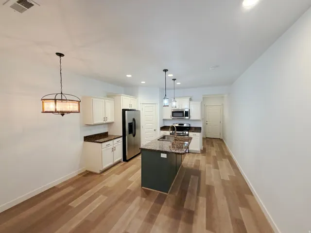 Open-concept kitchen and dining area featuring wood-finish flooring, recessed lighting, and a decorative dining pendant