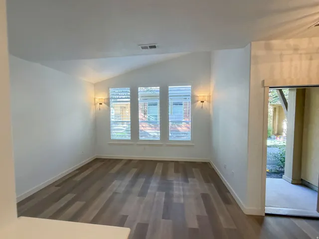 Spacious room featuring vaulted ceilings, wood-finish flooring, and multiple windows with plantation shutters
