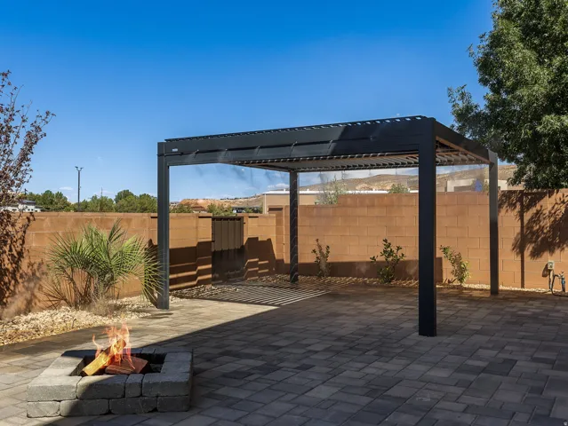 Pavered patio with a built-in fire pit, surrounded by a block wall, and featuring a modern pergola structure