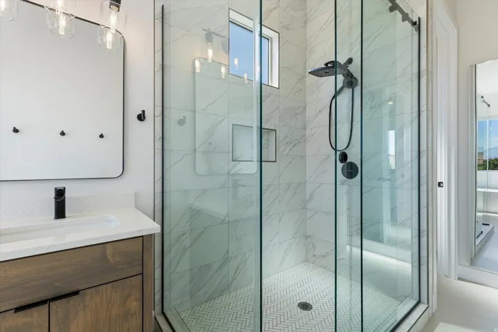 Contemporary bathroom featuring a glass-enclosed shower with matte black fixtures, marble-look tiled walls, and a herringbone-patterned shower floor