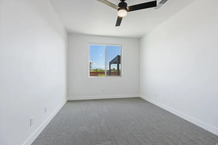 Bright interior space featuring a large window, neutral wall tones, modern ceiling fan, and carpeted flooring