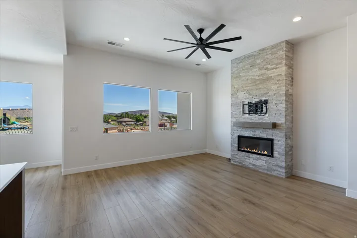 Open concept living space featuring a stacked stone fireplace with a floating wood mantle, a modern ceiling fan, recessed lighting, wood-finish flooring, and multiple windows