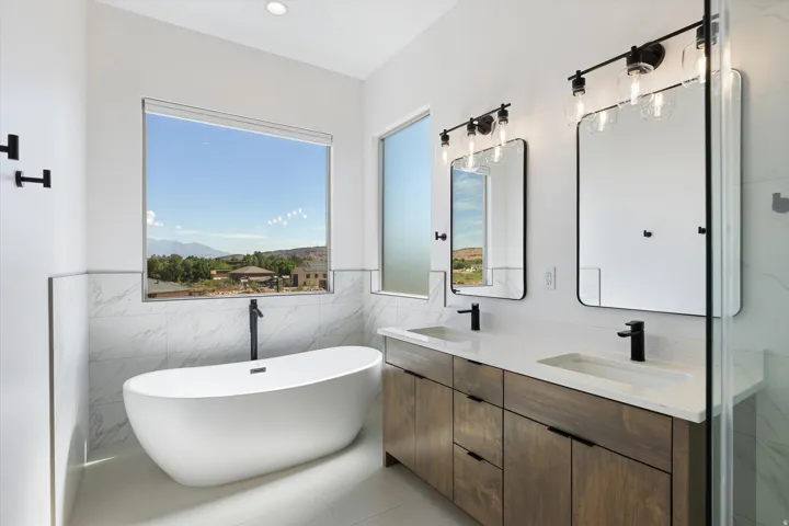 Modern bathroom featuring a freestanding soaking tub, large picture window, dual vanity with wood-finish cabinetry, quartz countertops, and matte black fixtures