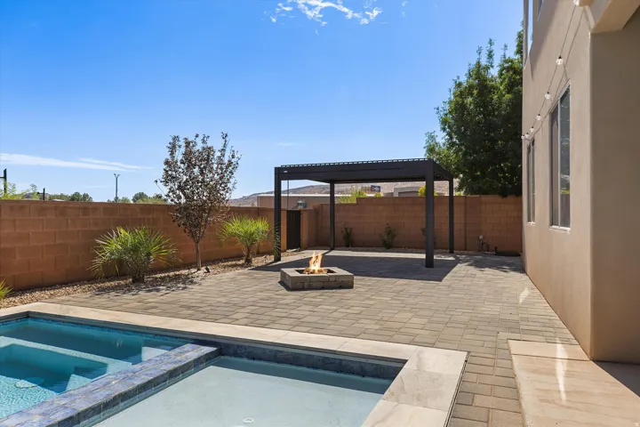 Spacious paved patio featuring a built-in fire pit, pergola, and integrated pool with an elevated spa
